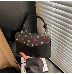 Detail of a black crossbody bag with floral pattern and elegant round top handle
