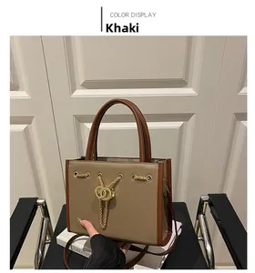 Detail view of khaki tote bag with gold chain ornament and dual ring lock on black chair