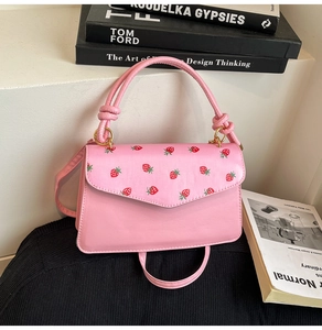 Pink crossbody bag with red strawberry print and elegant knot handle detail on steps