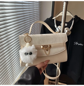Detail of cream flap crossbody bag with marble texture, golden triangle lock and cat charm