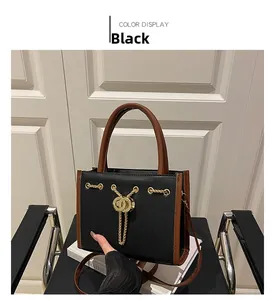 Detail of black pebbled leather tote bag with gold chain tassel and brown trim