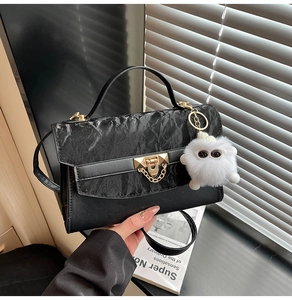 Detail of black flap bag with rock texture, golden chain lock and white fur pompom charm