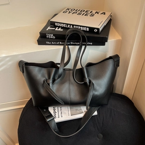 Minimalist black pleated tote bag with wide strap on a textured seat in a modern interior