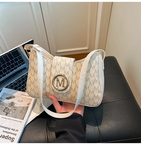 Macro detail of creamy faux leather bag featuring brown M pattern and gold M buckle