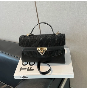 Detail view of black handbag with pleated flap texture and golden geometric clasp buckle