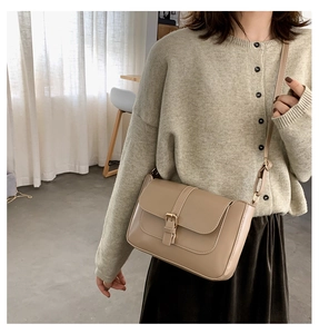 Model wearing a minimalist beige leather crossbody bag with vintage gold metal buckle