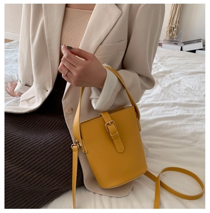 Detail view of mustard yellow bucket bag with metallic buckle and leather strap