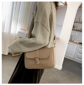 Detail of a retro beige crossbody bag featuring adjustable straps and metal buckle accent
