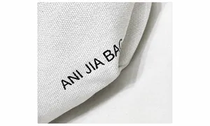 Detail van witte canvas textuur en zwarte ANI JIA BAG geprinte tekst op de tas