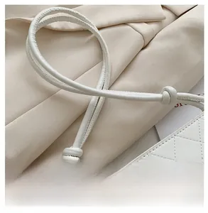 Détail du sac seau blanc matelassé avec une élégante bandoulière à nœuds en cuir souple