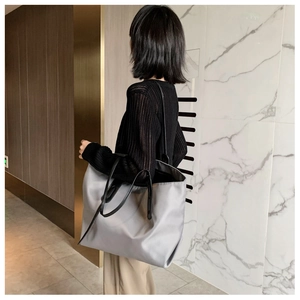 Detail view of a large grey tote bag with black leather straps on model shoulder