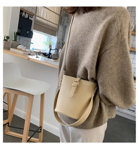 Detail of cream bucket bag with decorative leather buckle and slim shoulder strap