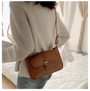 Brown leather crossbody bag shown on model in a cozy bright room setting with a warm vibe