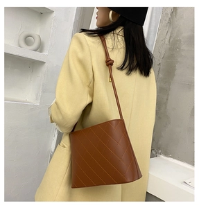 Dettaglio di una borsa a secchiello trapuntata marrone con tracolla annodata su blazer