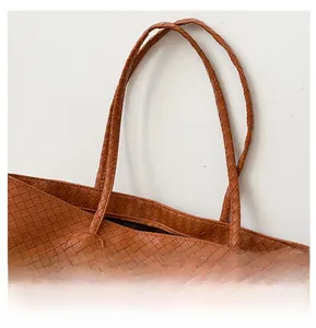 Detail of a brown woven leather tote bag featuring slim round straps and a metal zipper