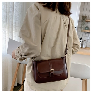 Detail of a dark brown vintage crossbody bag with a matte leather finish and buckle flap