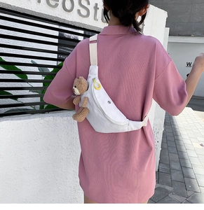 Outdoor street shot of a white canvas chest bag featuring a cute brown plush bear detail