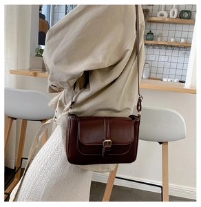 Detail of dark brown leather crossbody bag with metal buckle and matte texture