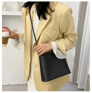 Sac seau matelassé noir porté par un mannequin en blazer jaune et jupe plissée