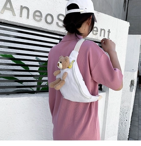 Close-up of white canvas chest bag featuring a 3D plush bear on adjustable beige strap