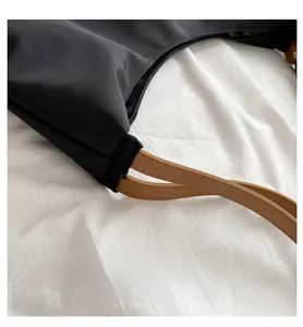 Close-up of black nylon shoulder bag with brown leather strap and fine stitching details