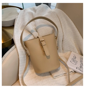 Close-up of beige leather bucket bag with top handle and adjustable strap on tweed fabric