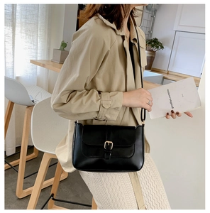 Close-up of a black leather crossbody bag with a gold buckle and adjustable strap detail