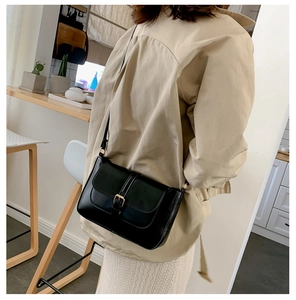 Detail of a minimalist black leather crossbody bag with a gold buckle worn by a model