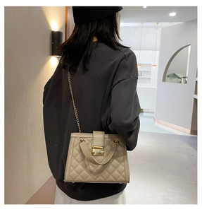 Dettaglio borsa trapuntata beige con chiusura girevole dorata e tracolla a catena su modella