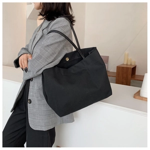 Detail view of large black canvas tote bag showing the golden metal snap button closure