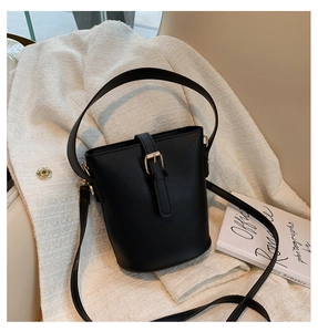 Close-up of black bucket bag with gold buckle on textured fabric and book background