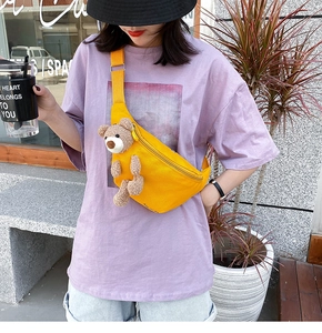 Detail of yellow canvas chest bag featuring a 3D plush bear doll and adjustable strap