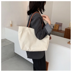 Detail shot of oversized beige canvas tote bag with brown leather handles on shoulder