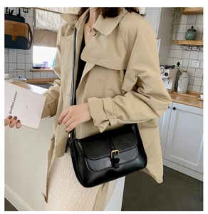 Minimalist black leather crossbody bag with gold buckle on model in beige trench coat