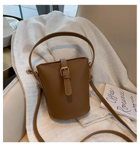 Detail view of brown leather bucket bag with gold buckle on textured background
