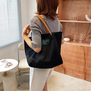 Large black canvas tote bag with brown handles shown in a modern home office setting