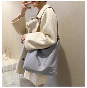 Close-up of lightweight grey nylon hobo shoulder bag with brown leather straps on model
