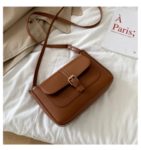 Detailed macro view of brown PU leather shoulder bag with gold buckle on white fabric