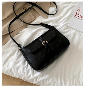 Close-up of black matte leather shoulder bag with metallic buckle and adjustable strap