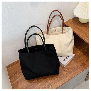 Detail of canvas tote bags with leather handles and magnetic snap closure on a wooden shelf