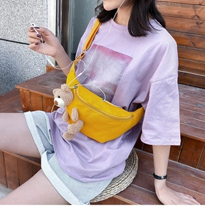 Detailed outdoor view of a bright yellow canvas chest bag with a cute brown teddy bear plush