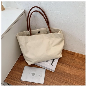 Detail view of large canvas tote bag with brown leather handles and magnetic snap closure