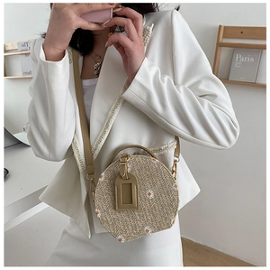 Détail d'un sac rond en paille avec broderie marguerite blanche et bandoulière en cuir