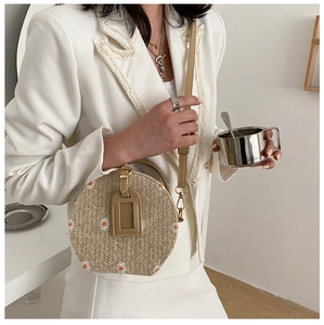 Détail d'un sac à bandoulière rond tissé beige avec broderie florale marguerite
