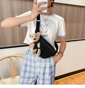 Close-up of black canvas chest bag featuring a cute plush bear doll with adjustable strap