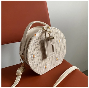 Détail du sac rond en paille tissée avec broderie de marguerites et bandoulière en cuir crème