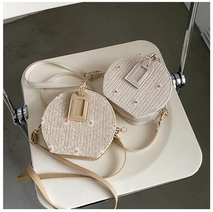 Détail du sac à bandoulière rond en paille tressée avec broderie de marguerites et lanière