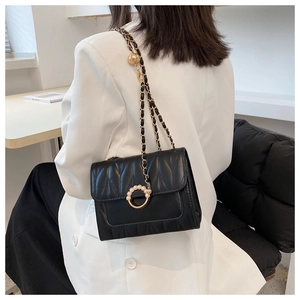Détail d'un sac bandoulière noir matelassé avec chaîne dorée et boucle à perles élégante