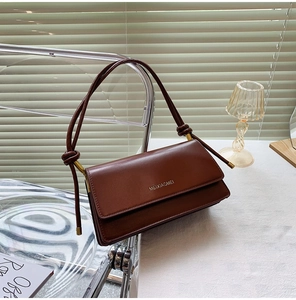 Detail of deep brown leather bag with elegant knot strap and gold metal hardware