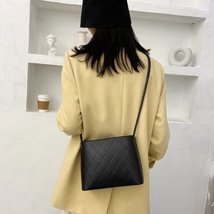 Sac seau matelassé noir classique avec bandoulière porté par un mannequin en décor épuré